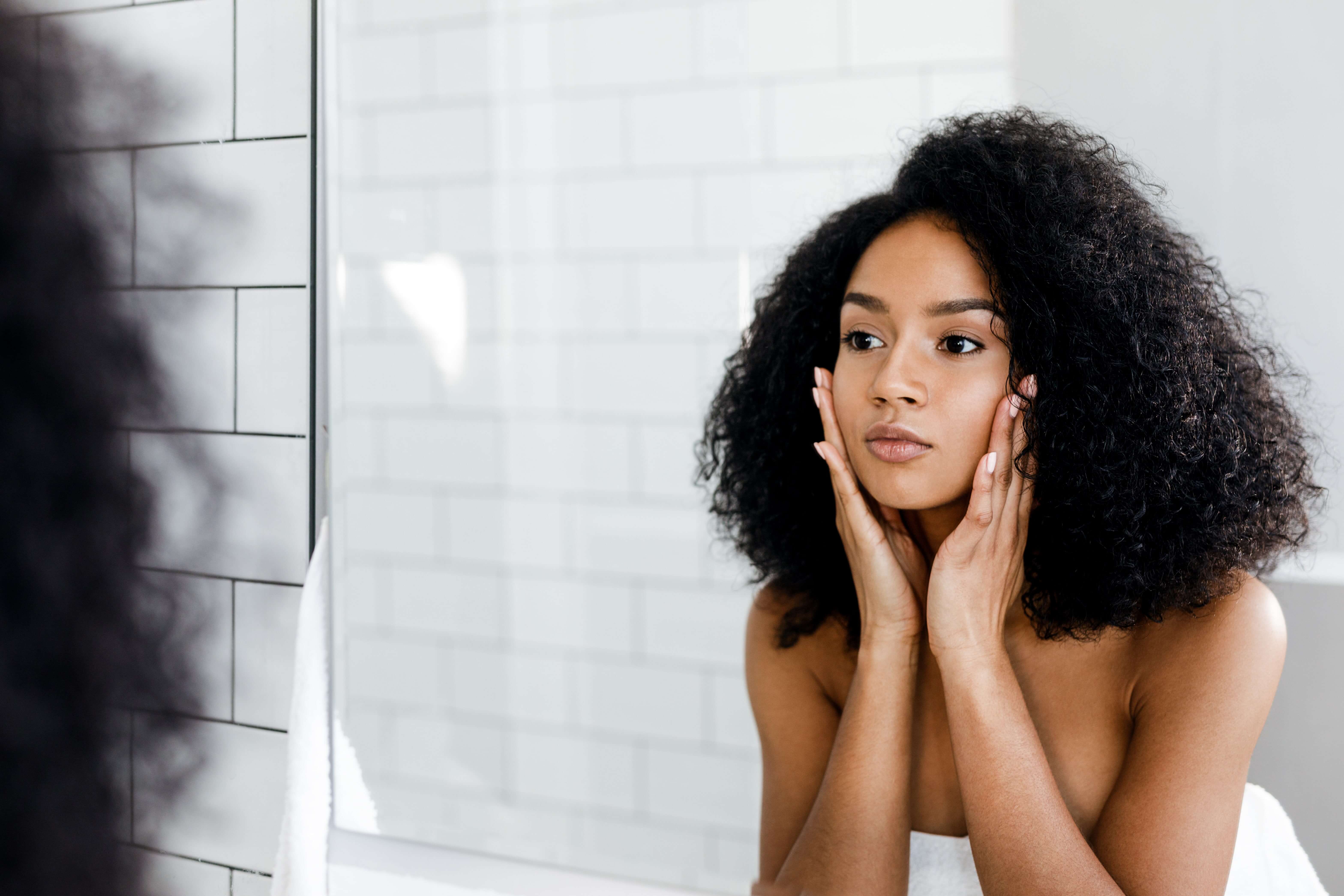 Woman looking in mirror after Acne Scar Treatment